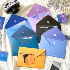 Set thiệp kèm phong bì với nhiều màu sắc khác nhau, bao gồm màu tím, xanh, đen, vàng và xanh lơ, với hình ảnh của trăng, núi và biển.